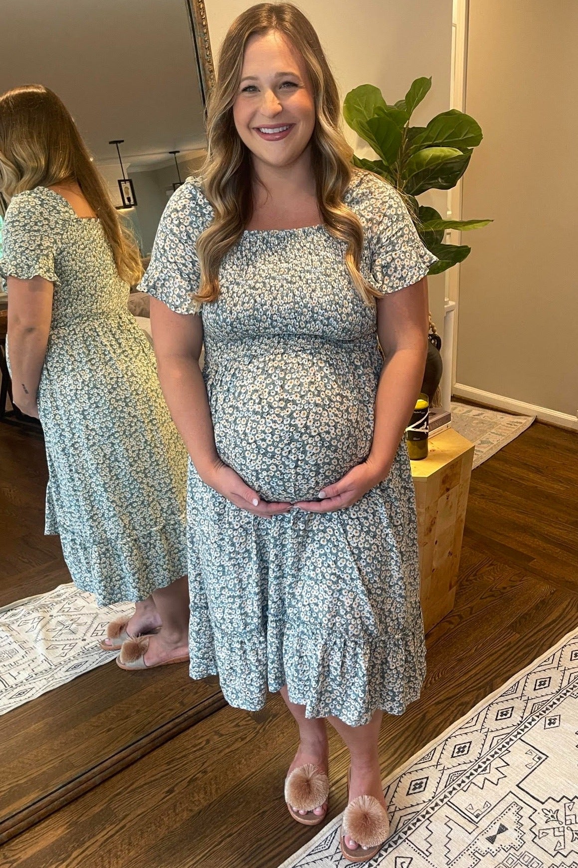 woman wearing a light blue floral maternity dress and holding her baby bump
