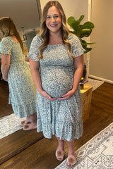 woman wearing a light blue floral maternity dress and holding her baby bump