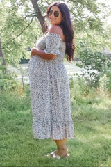 woman wearing a floral off-the-shoulder maternity dress and showing her baby bump in a natural outdoor setting