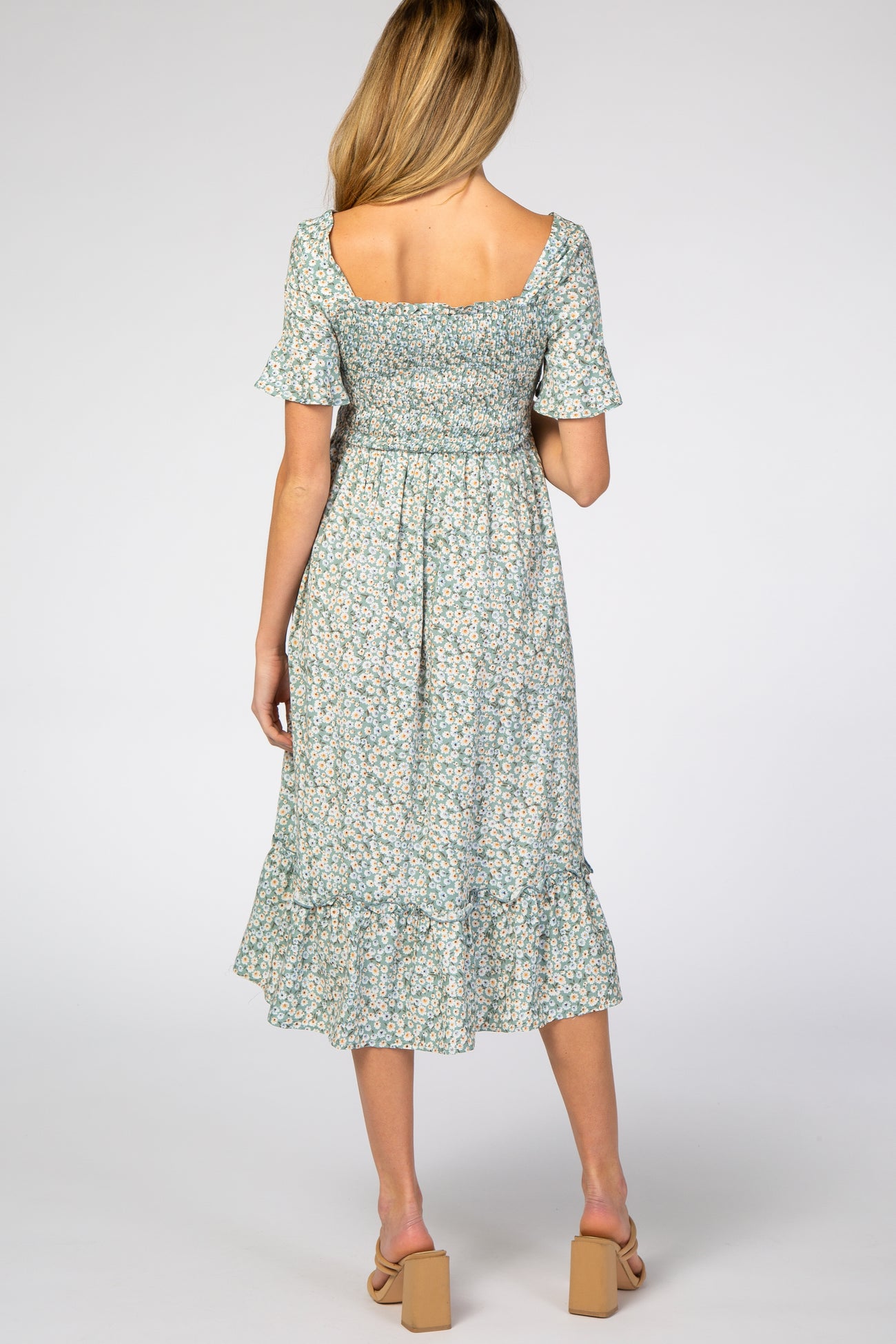 woman wearing a light blue floral maternity dress with short sleeves and a ruffled hem, showing a baby bump from the back