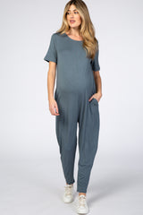 woman wearing a teal short sleeve maternity jumpsuit with side pockets and a visible baby bump