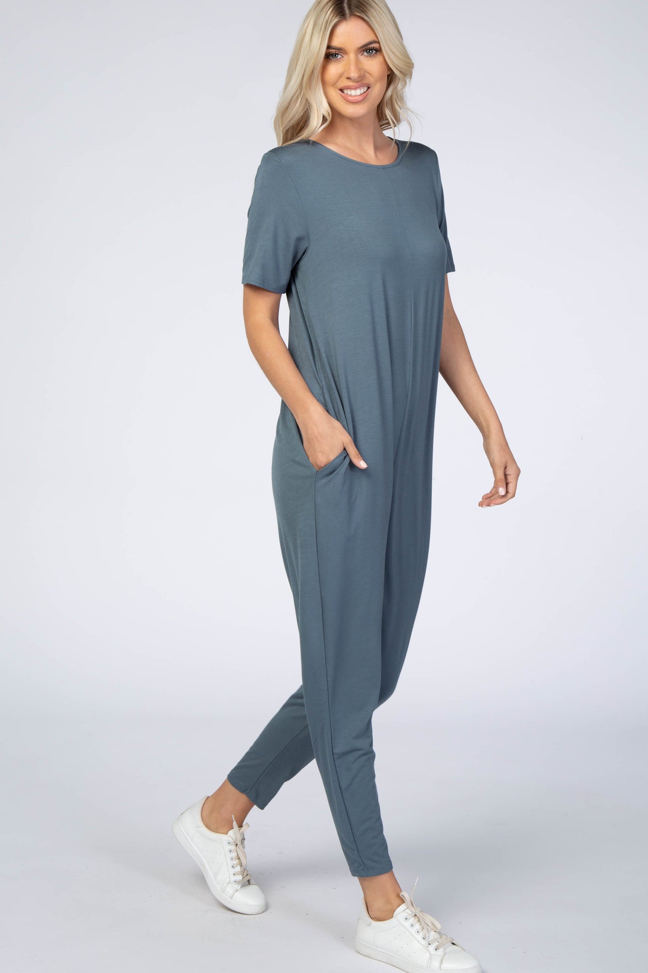 woman wearing a loose-fit dark teal jumpsuit with short sleeves and pockets, paired with white sneakers