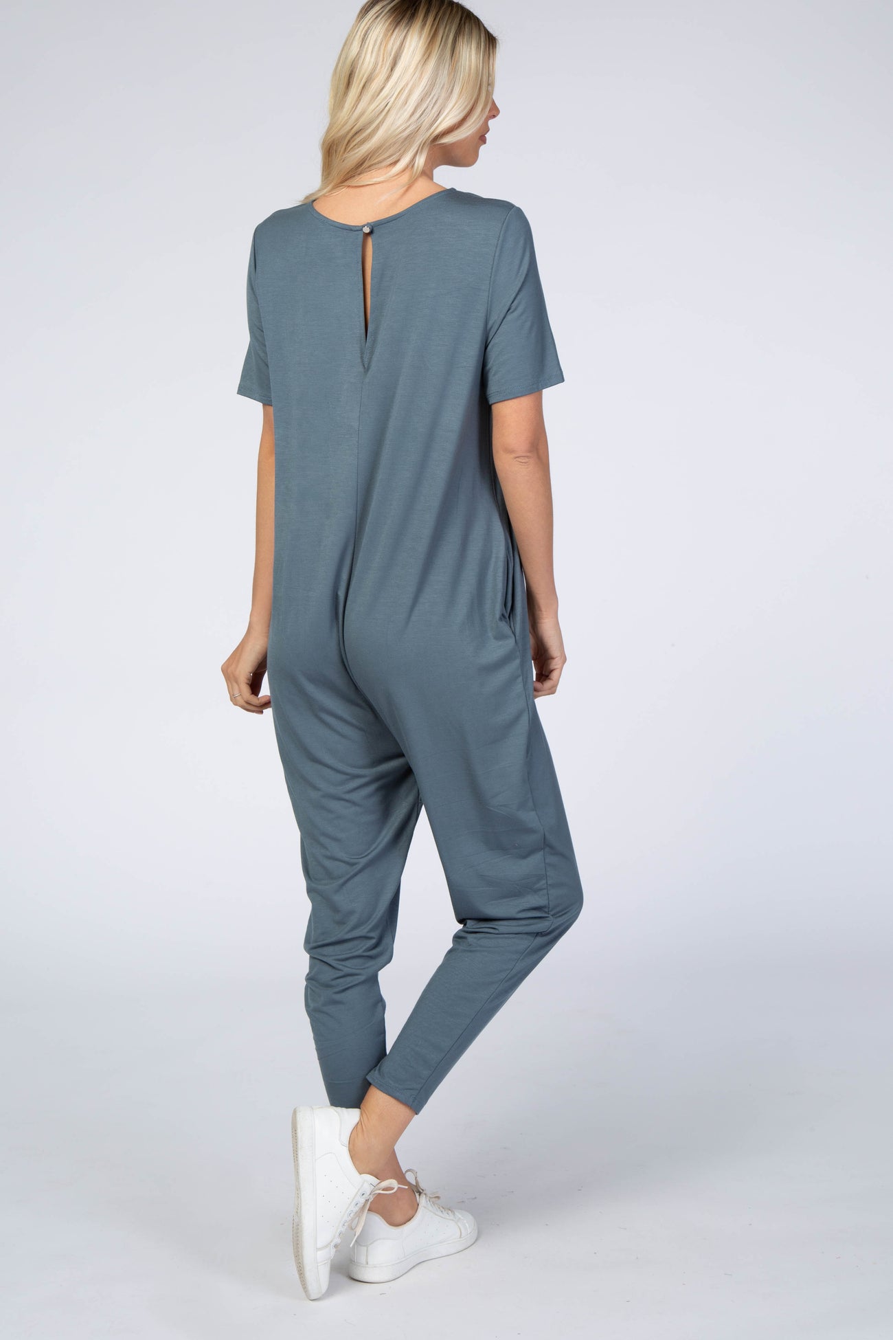 back view of a woman wearing a short sleeve slate blue maternity jumpsuit with white sneakers