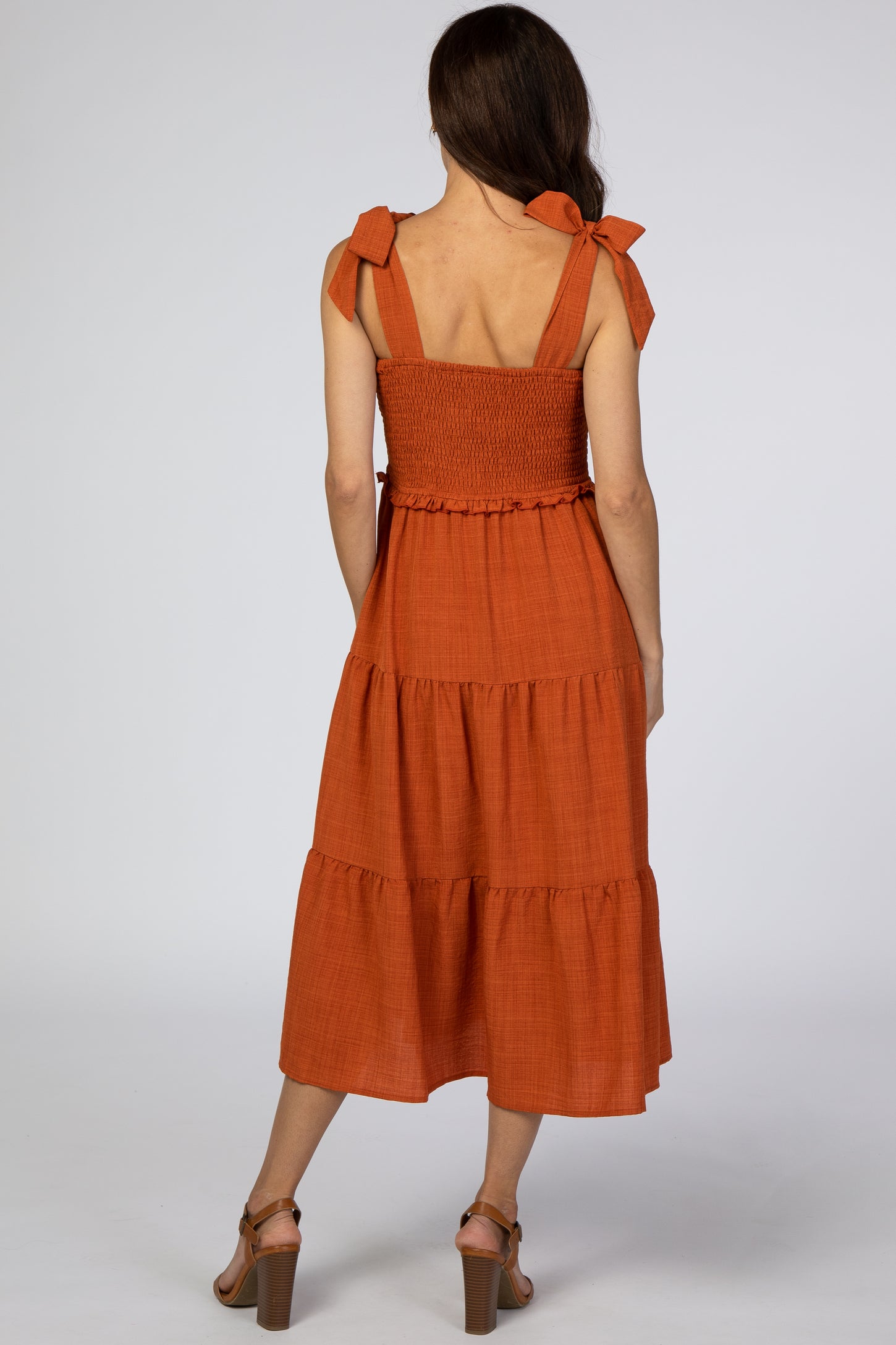 woman wearing a rust-colored tiered midi dress with tie straps and a smocked bodice, seen from the back