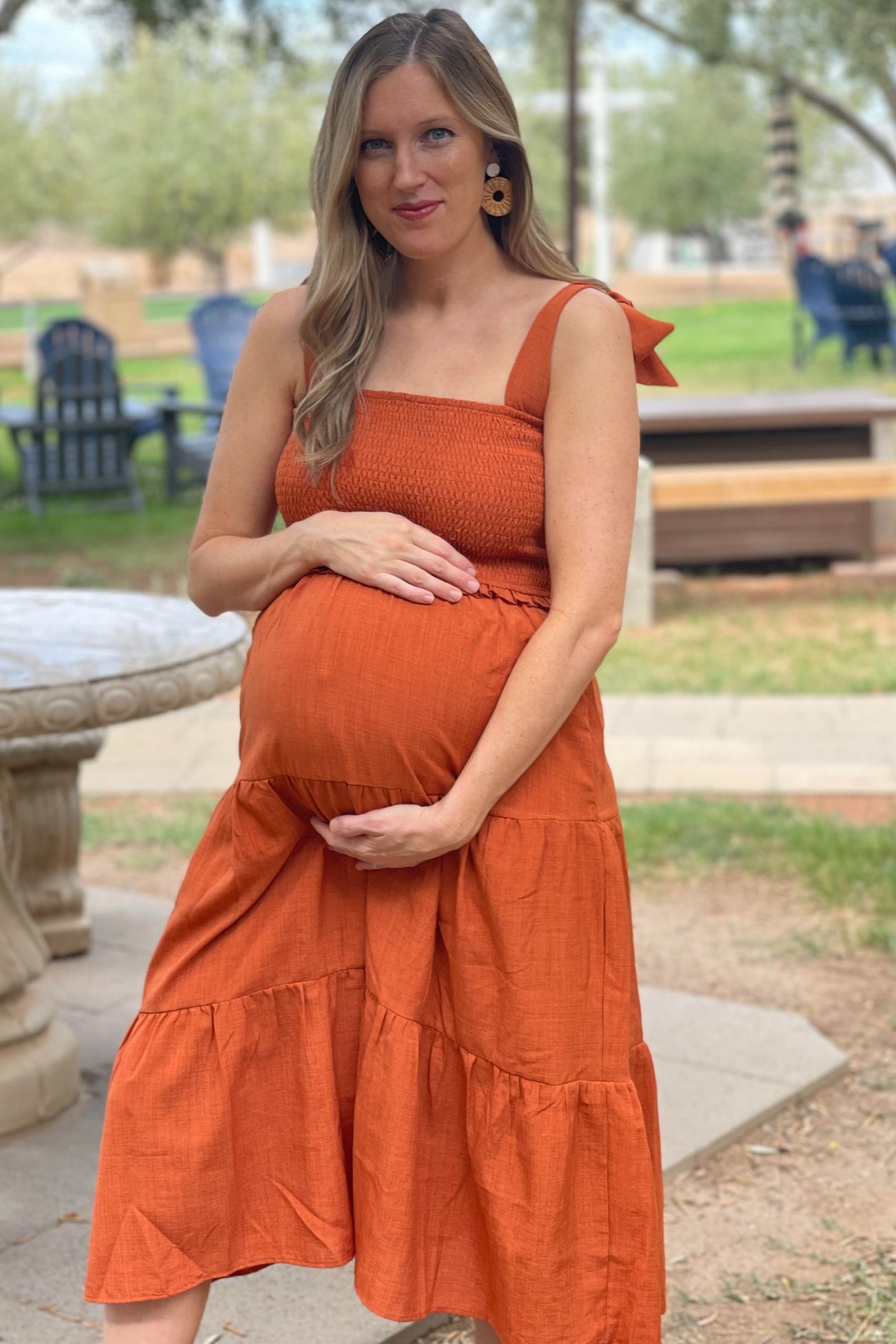 woman wearing an orange maternity dress with smocked bodice and tiered skirt, holding her baby bump