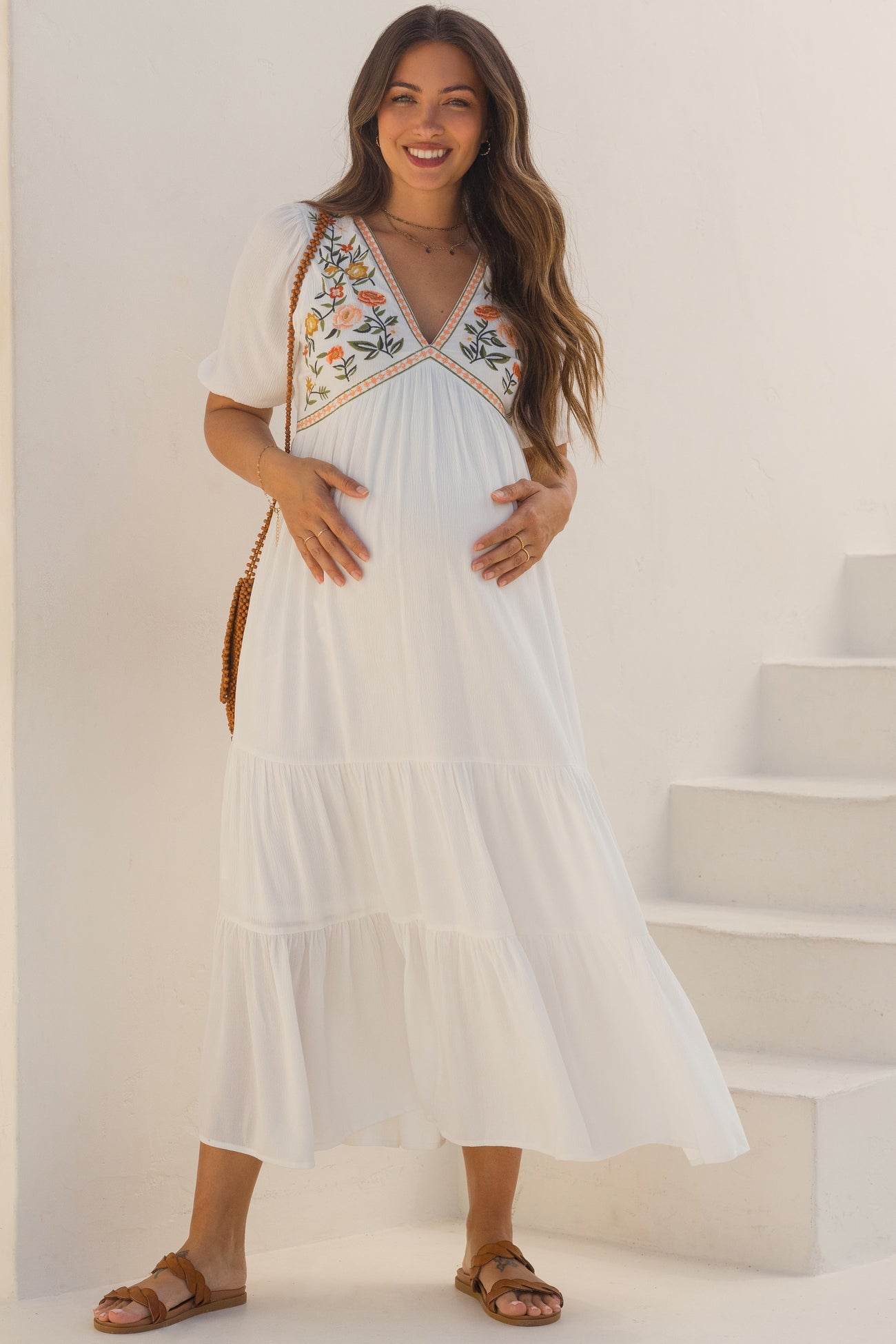 woman wearing a white maternity maxi dress with floral embroidery and a visible baby bump
