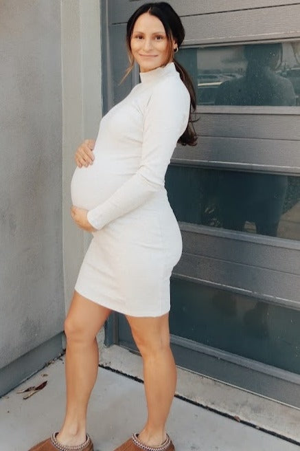 woman wearing a white long sleeve maternity dress and holding her baby bump