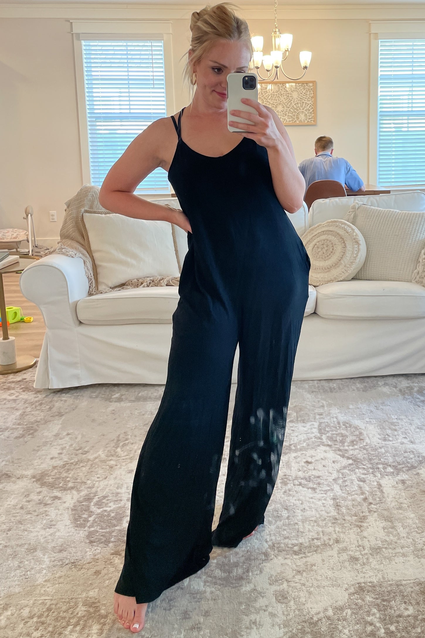 woman wearing a black sleeveless jumpsuit with a loose fit, posing in front of a mirror