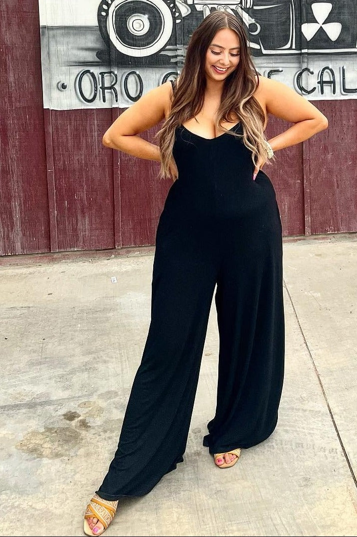 woman wearing a black sleeveless jumpsuit with wide legs, standing confidently outdoors