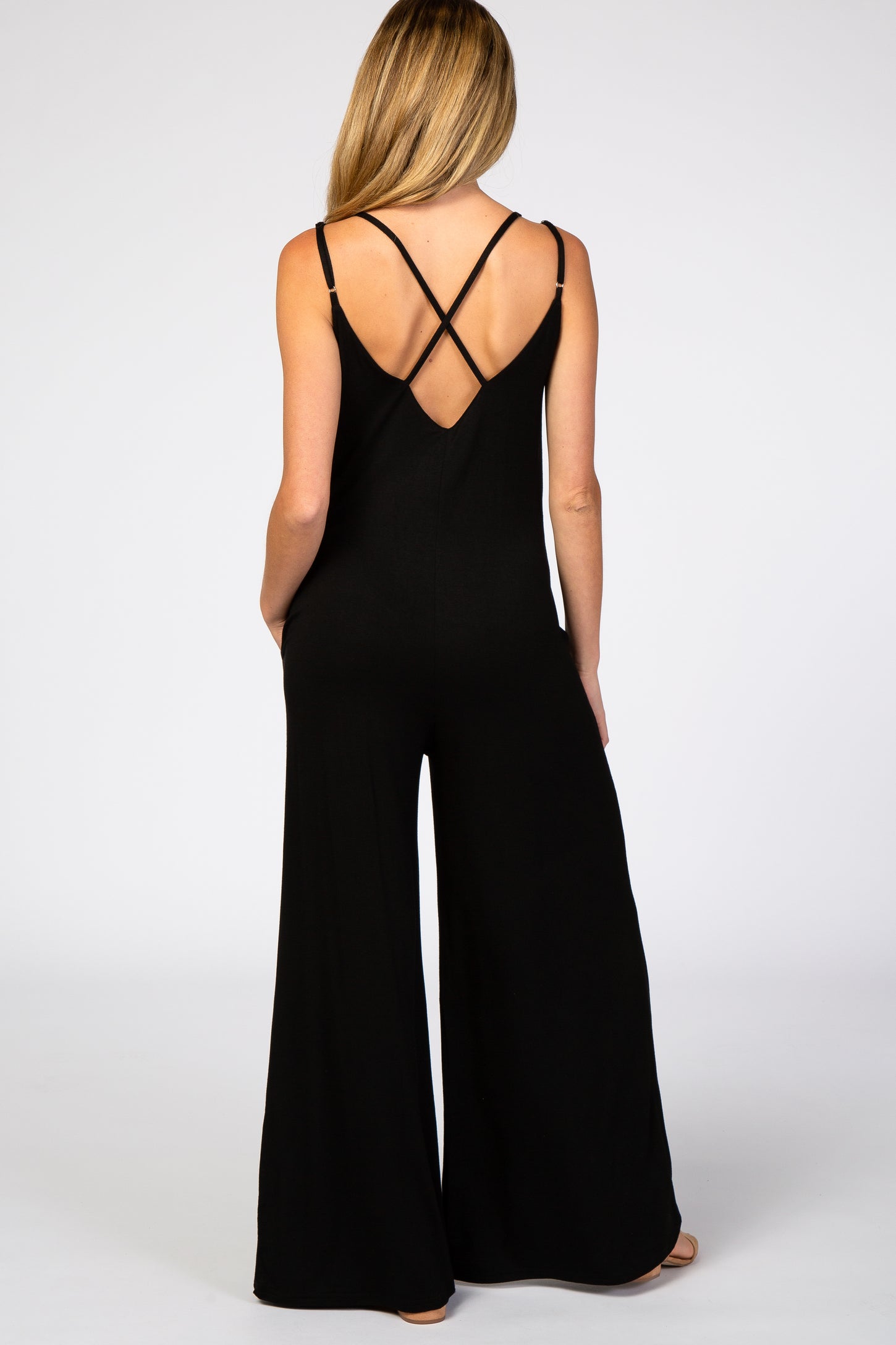 woman wearing a black maternity jumpsuit with crisscross straps and a wide leg silhouette, back view