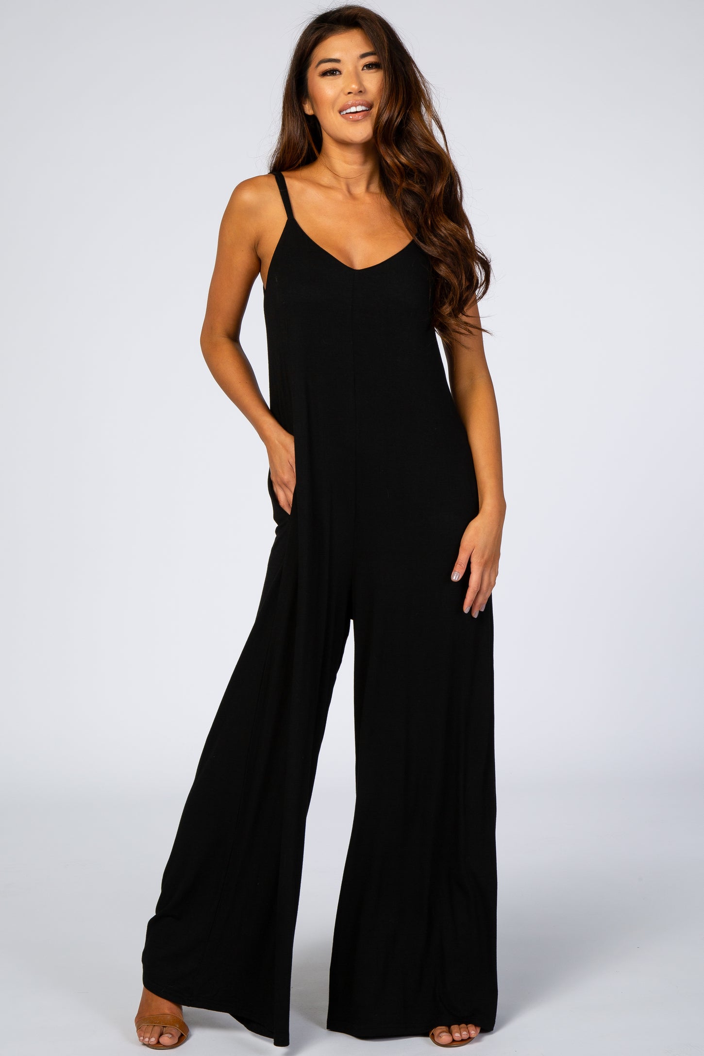 woman wearing a black sleeveless jumpsuit with wide legs and pockets, smiling at the camera