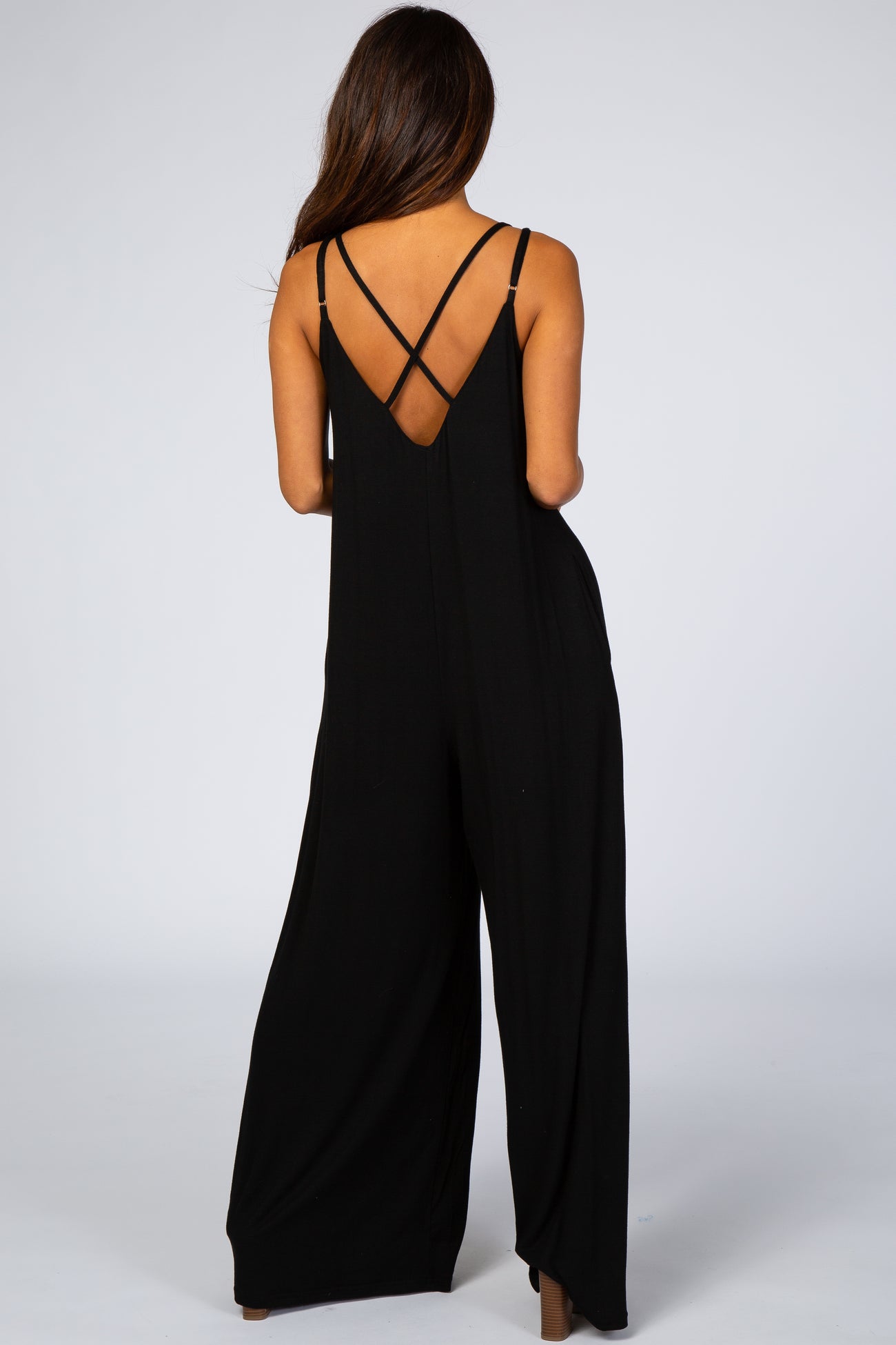 woman wearing a black sleeveless jumpsuit with crisscross back straps and wide legs