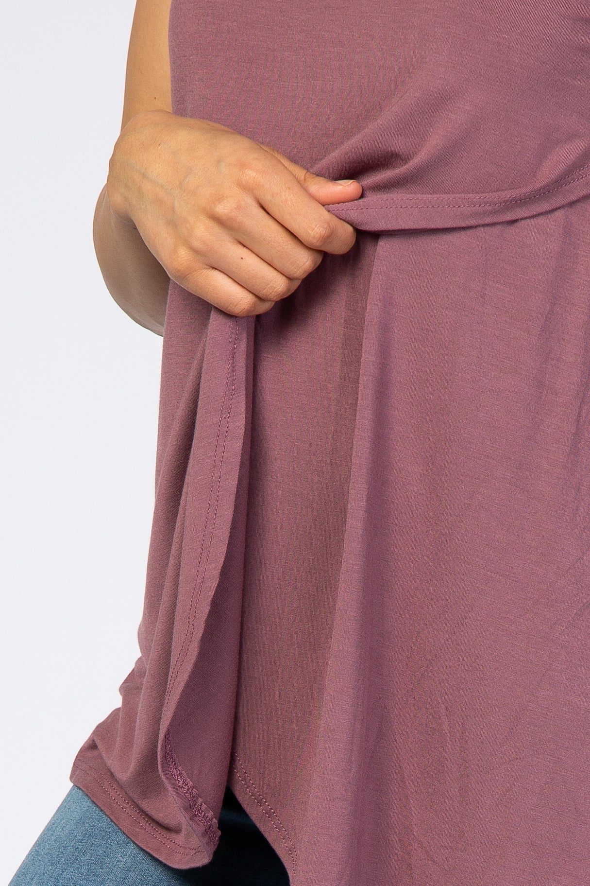 close-up of a woman’s hand holding the hem of a loose-fitting mauve top with a curved bottom edge