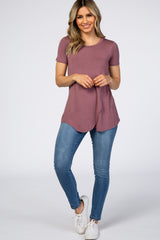 woman wearing a mauve short sleeve top with a curved hem and blue skinny jeans, standing against a plain background