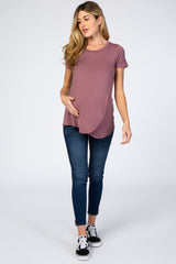 woman wearing a mauve short sleeve maternity top with a curved hem and holding her baby bump, paired with skinny jeans