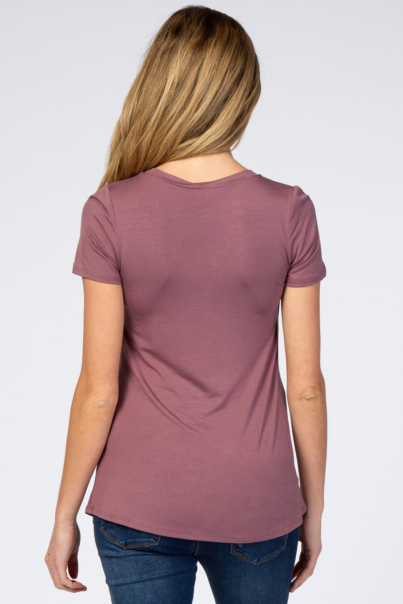 woman wearing a mauve short sleeve maternity top, viewed from the back, paired with blue jeans