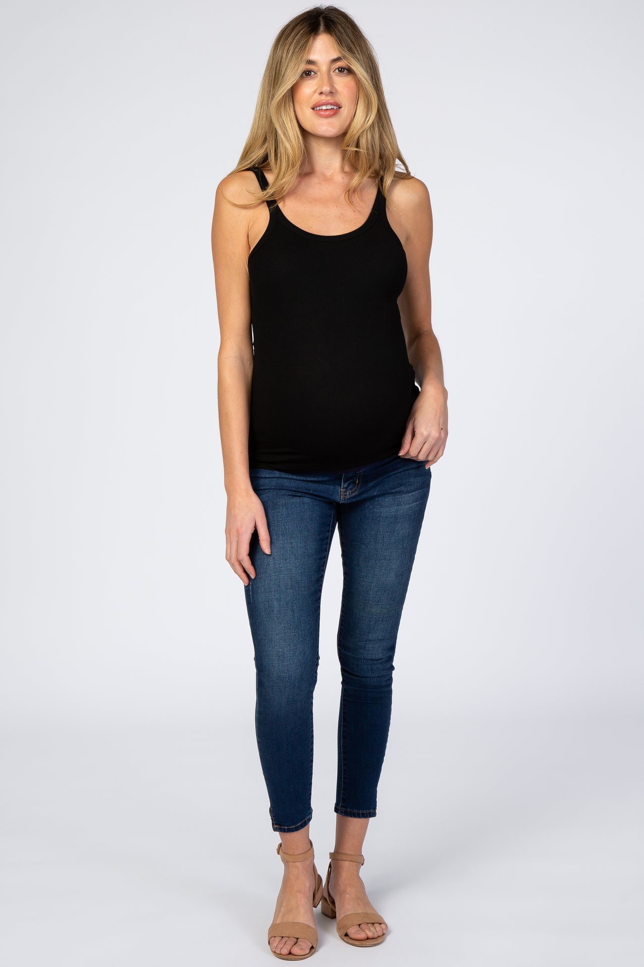 woman wearing a black maternity tank top and blue skinny jeans, showing her baby bump