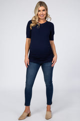 woman wearing a navy blue maternity top and blue skinny jeans, showing her baby bump