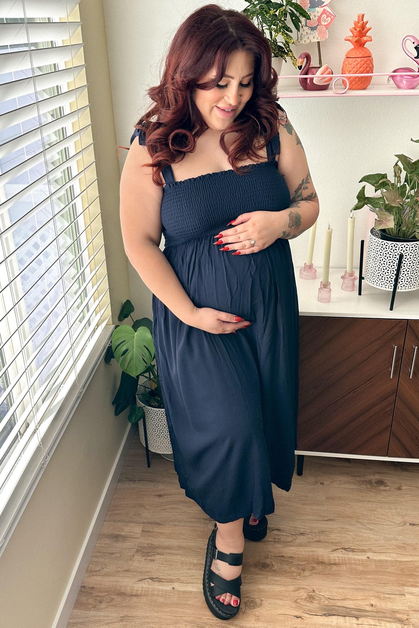 woman wearing a navy blue smocked maternity dress, standing and holding her baby bump