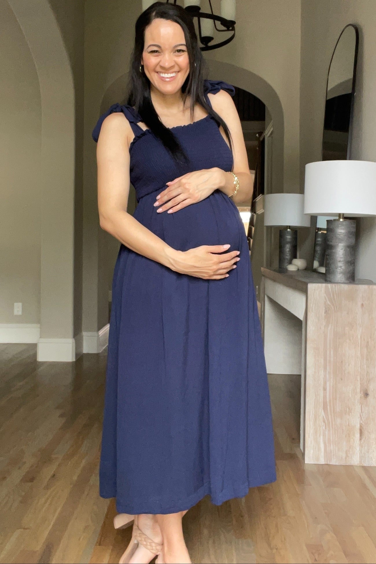 woman wearing a navy blue maternity dress with straps, smiling and holding her baby bump