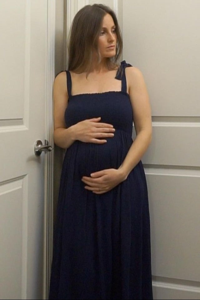woman wearing a dark navy maternity maxi dress with tie straps and holding her baby bump