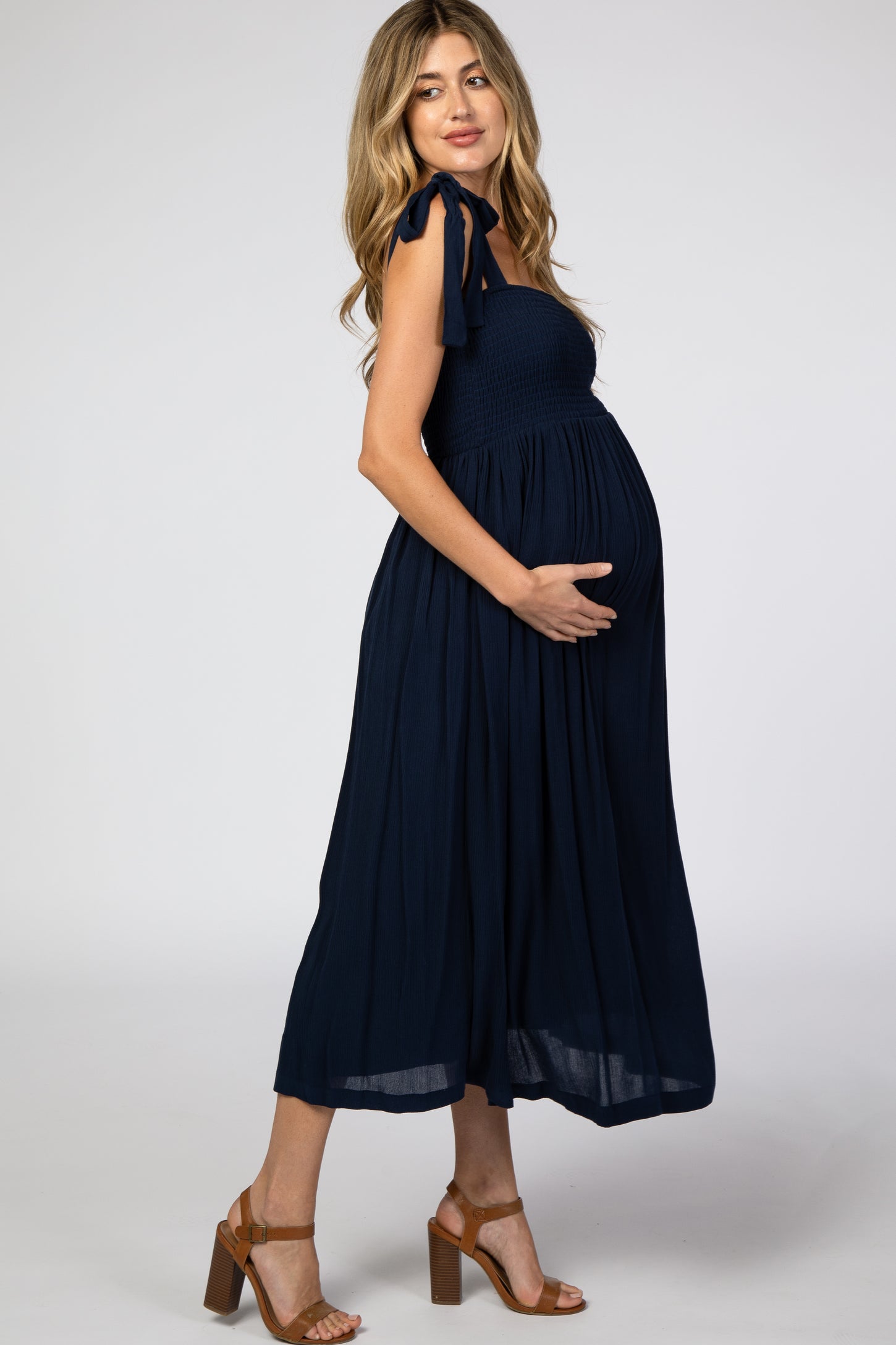 woman wearing a navy blue maternity maxi dress with shoulder ties and holding her baby bump