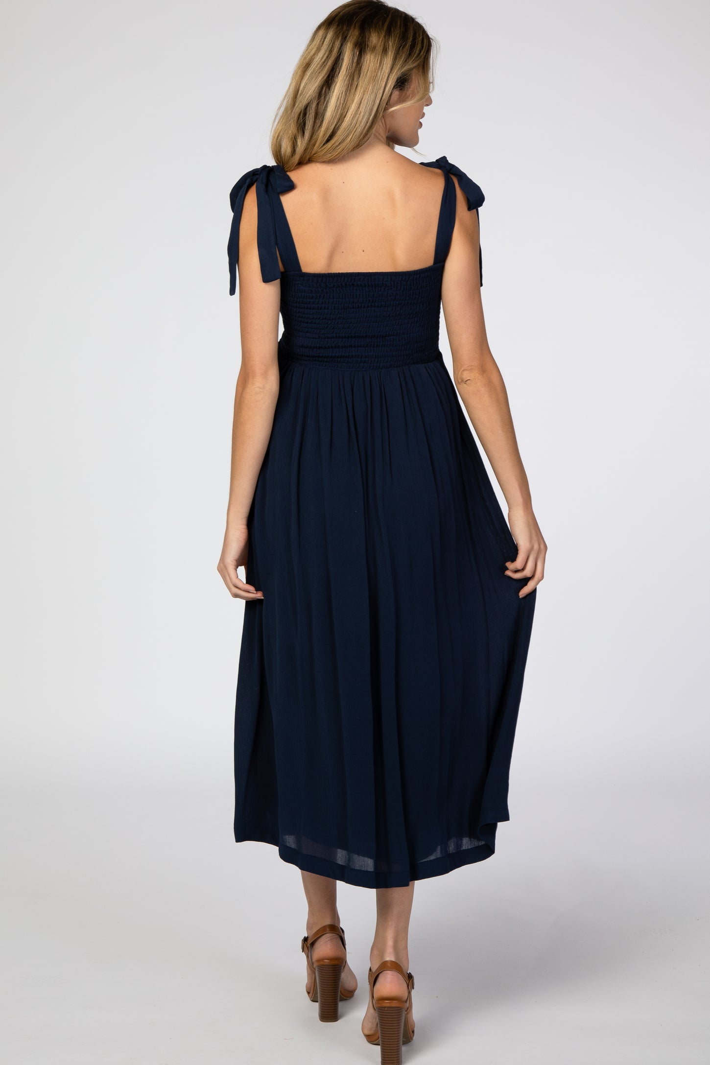 woman wearing a navy blue sleeveless maternity maxi dress with tie shoulder straps, showing a relaxed fit and flowing skirt