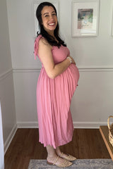 woman wearing a pink maternity dress with smocked bodice and holding her baby bump