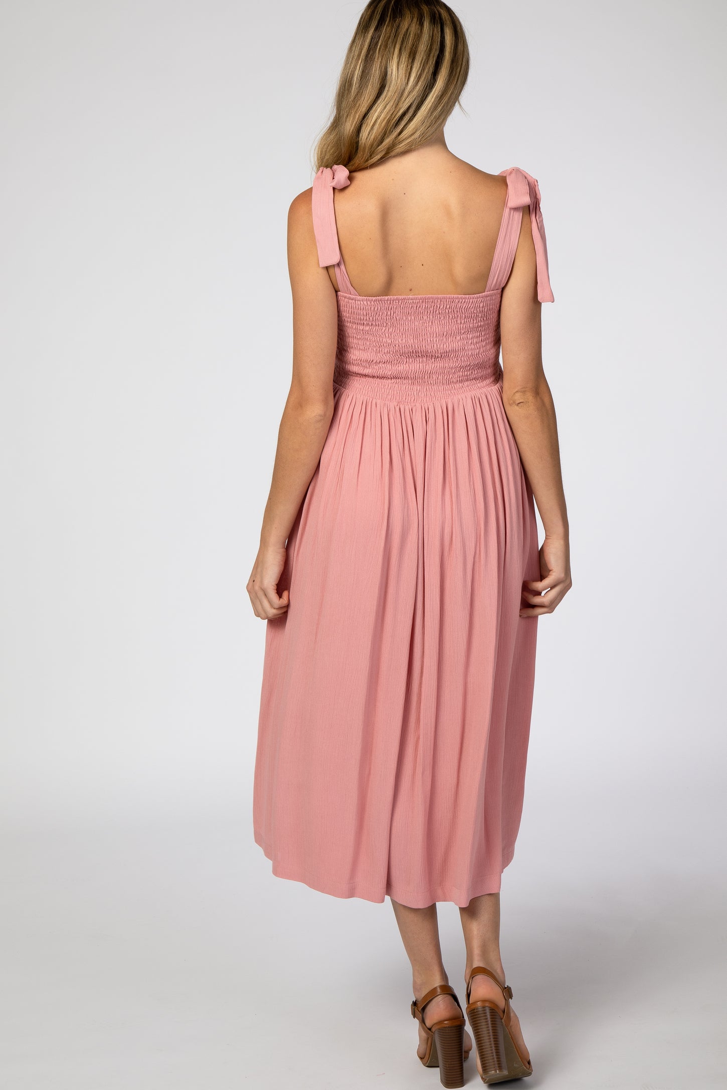 woman wearing a pink maternity dress with smocked bodice and tie straps, showing the back view