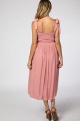 woman wearing a pink maternity dress with smocked bodice and tie straps, showing the back view