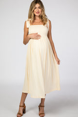 woman wearing a cream-colored maternity dress with tie straps and a visible baby bump