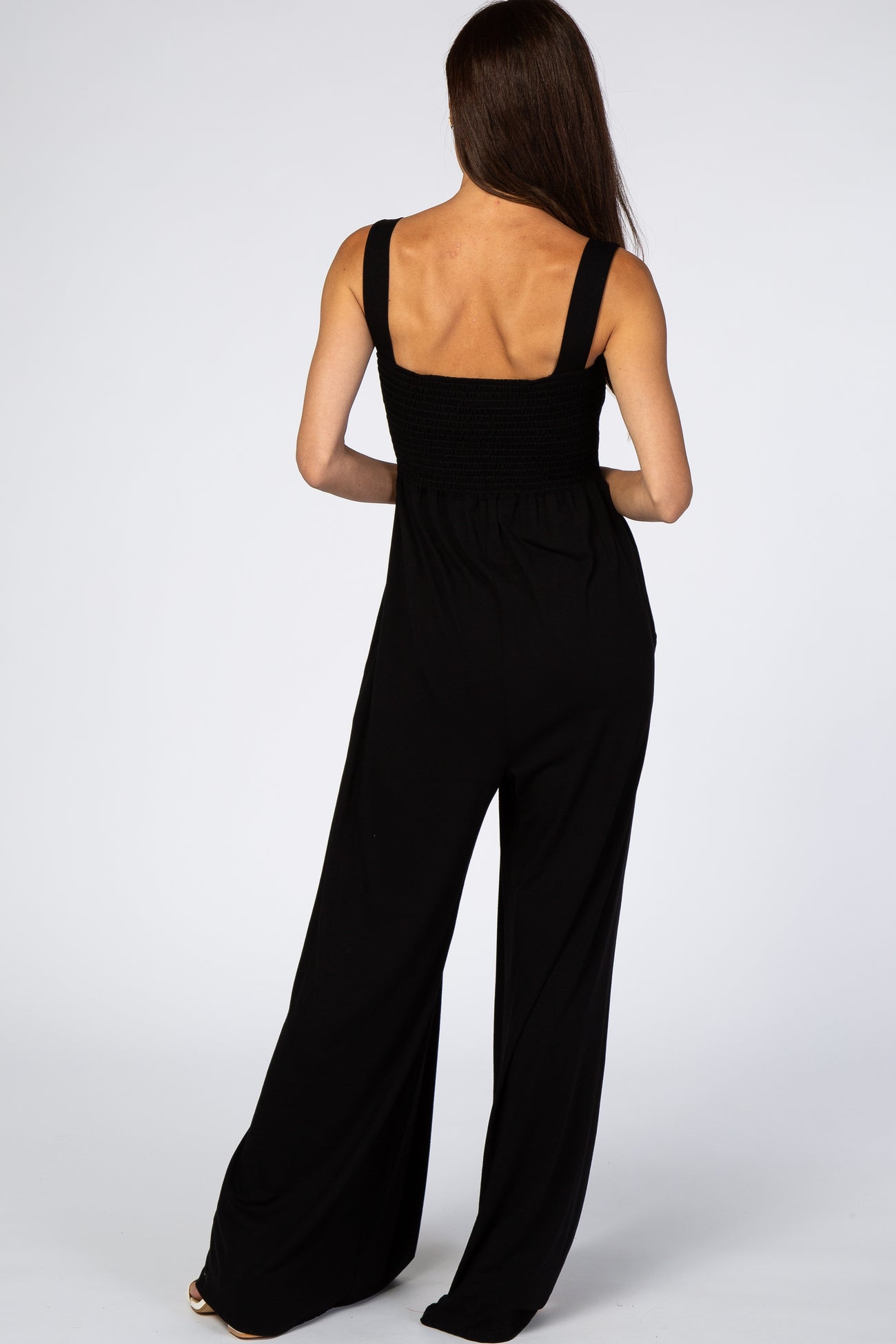 woman wearing a black sleeveless jumpsuit with a smocked bodice and wide-leg trousers, viewed from the back