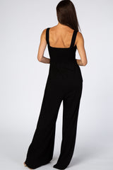 woman wearing a black sleeveless jumpsuit with a smocked bodice and wide-leg trousers, viewed from the back