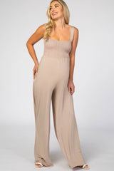 woman wearing a light brown maternity jumpsuit with a smocked bodice and wide legs, showcasing her baby bump