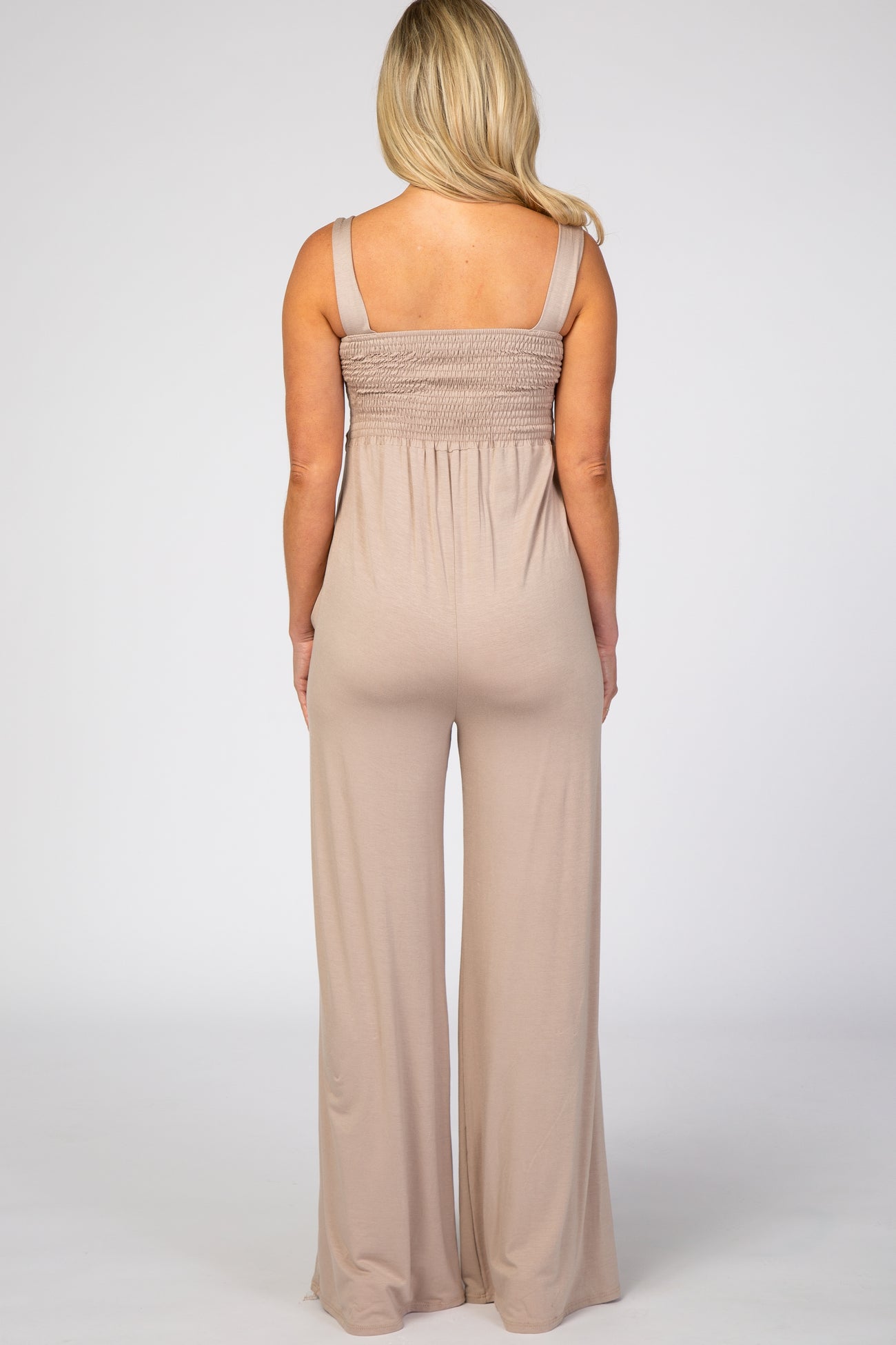 woman wearing a beige maternity jumpsuit with a smocked bodice and flowy wide legs, viewed from the back