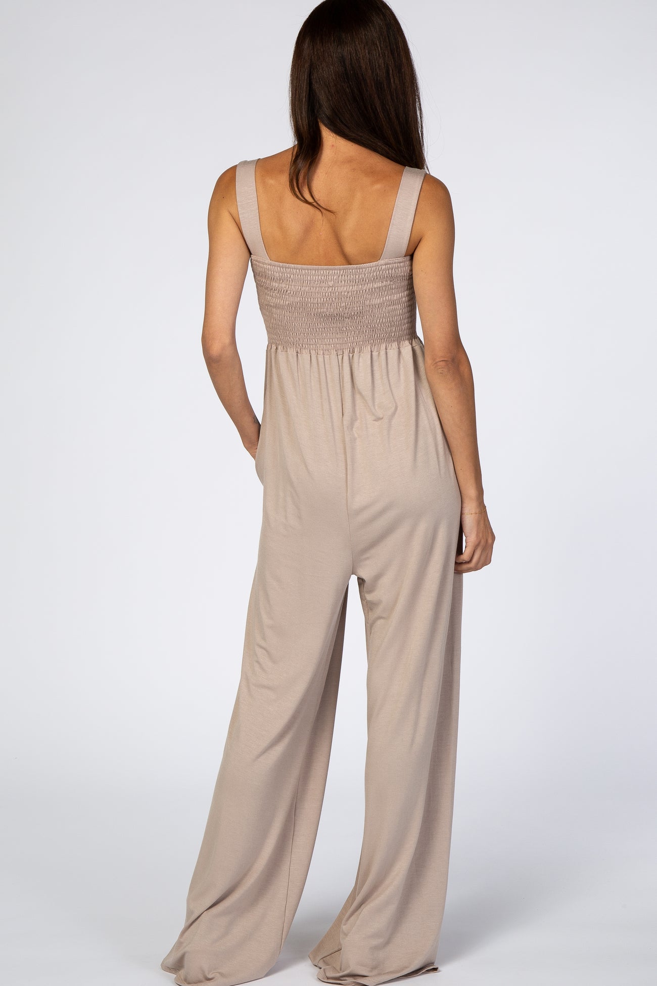 woman wearing a light brown smocked back jumpsuit with wide legs and spaghetti straps, shown from the back
