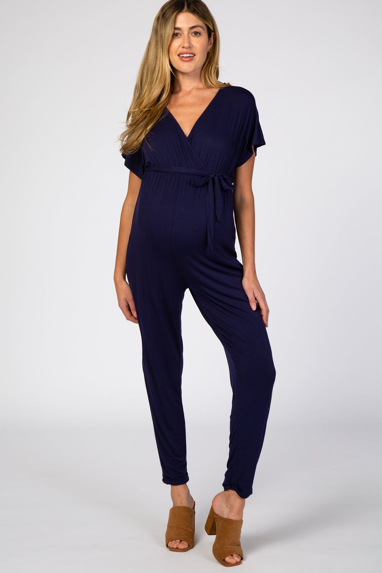 woman wearing a navy blue maternity jumpsuit with a tie waist and short sleeves, showcasing her baby bump