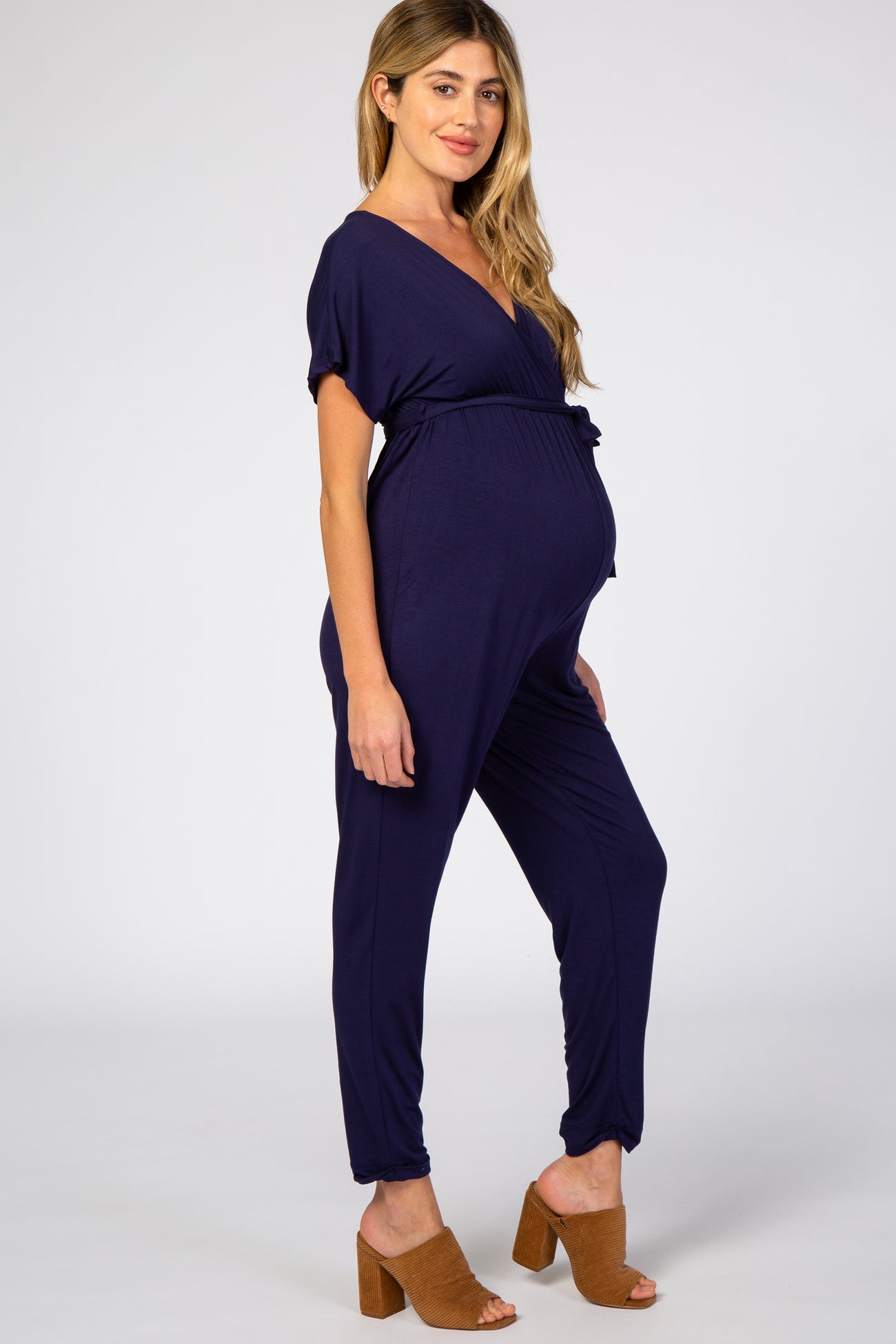 woman wearing a navy blue short sleeve maternity jumpsuit with a tie waist and visible baby bump