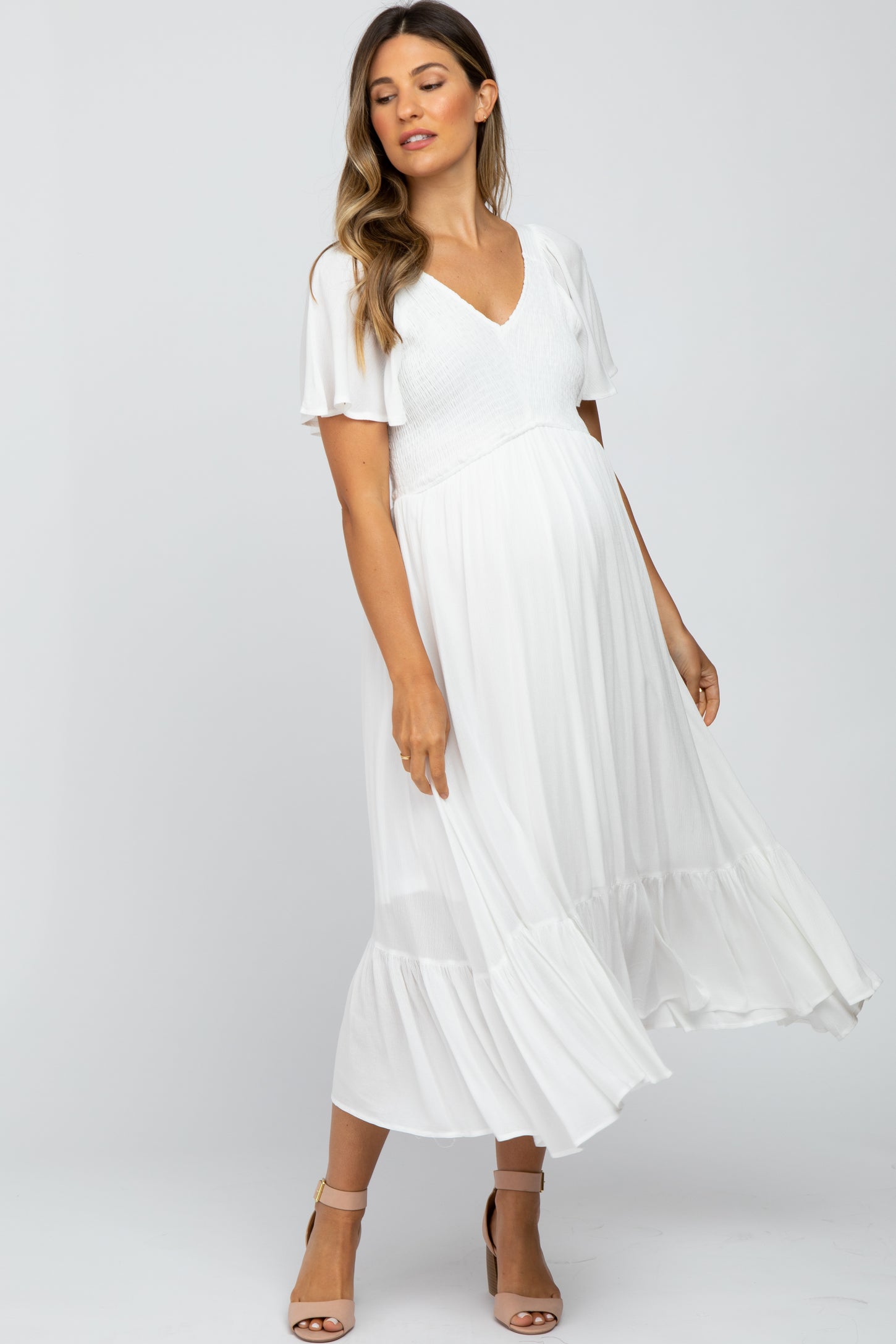 woman wearing a white maternity dress with a v-neck and flutter sleeves, showcasing her baby bump
