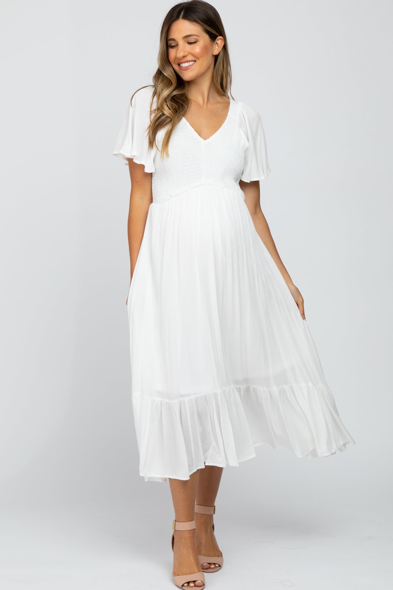 woman wearing a white maternity dress with flutter sleeves and a tiered hem, showcasing a baby bump
