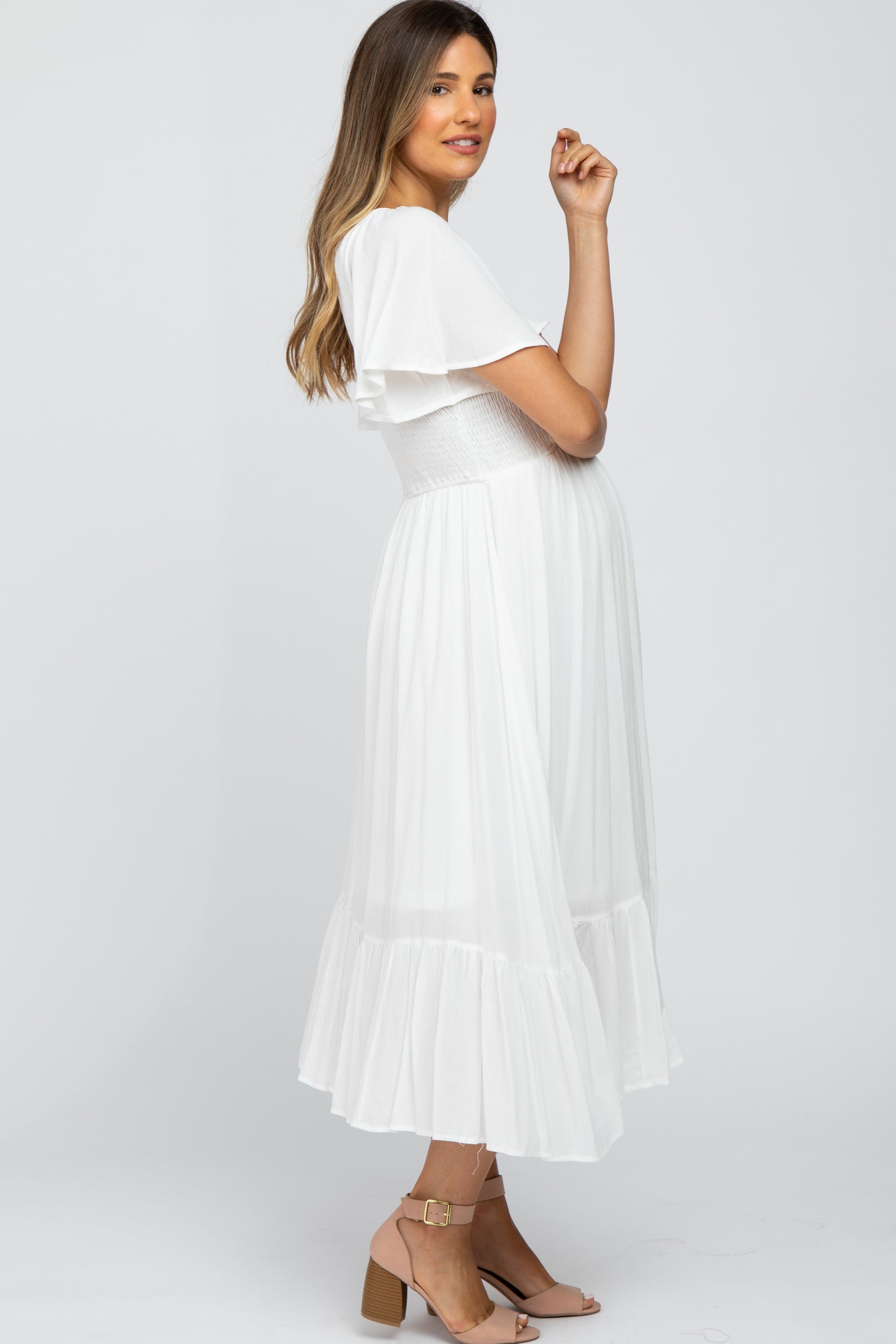 woman wearing a white maternity dress with flutter sleeves and a smocked bodice, showcasing her baby bump