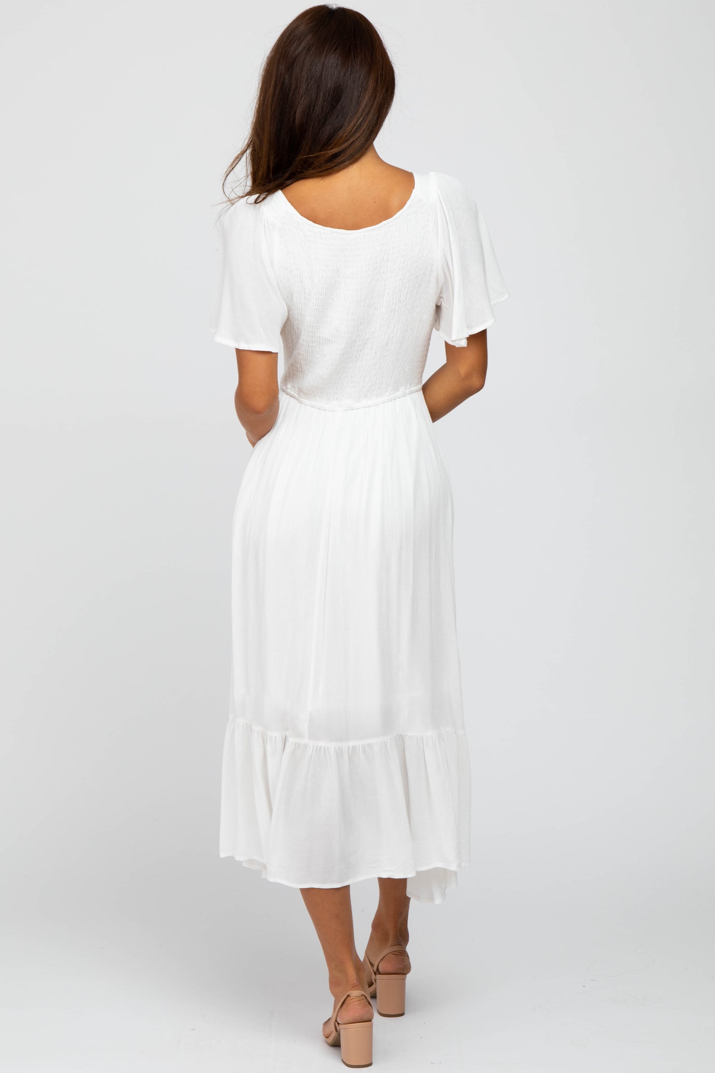 woman wearing a flowy white midi dress with short sleeves and a tiered hem, seen from the back