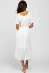 woman wearing a flowy white midi dress with short sleeves and a tiered hem, seen from the back