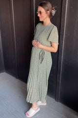 woman wearing a green floral maternity maxi dress with pleats and a tie waist, holding her baby bump