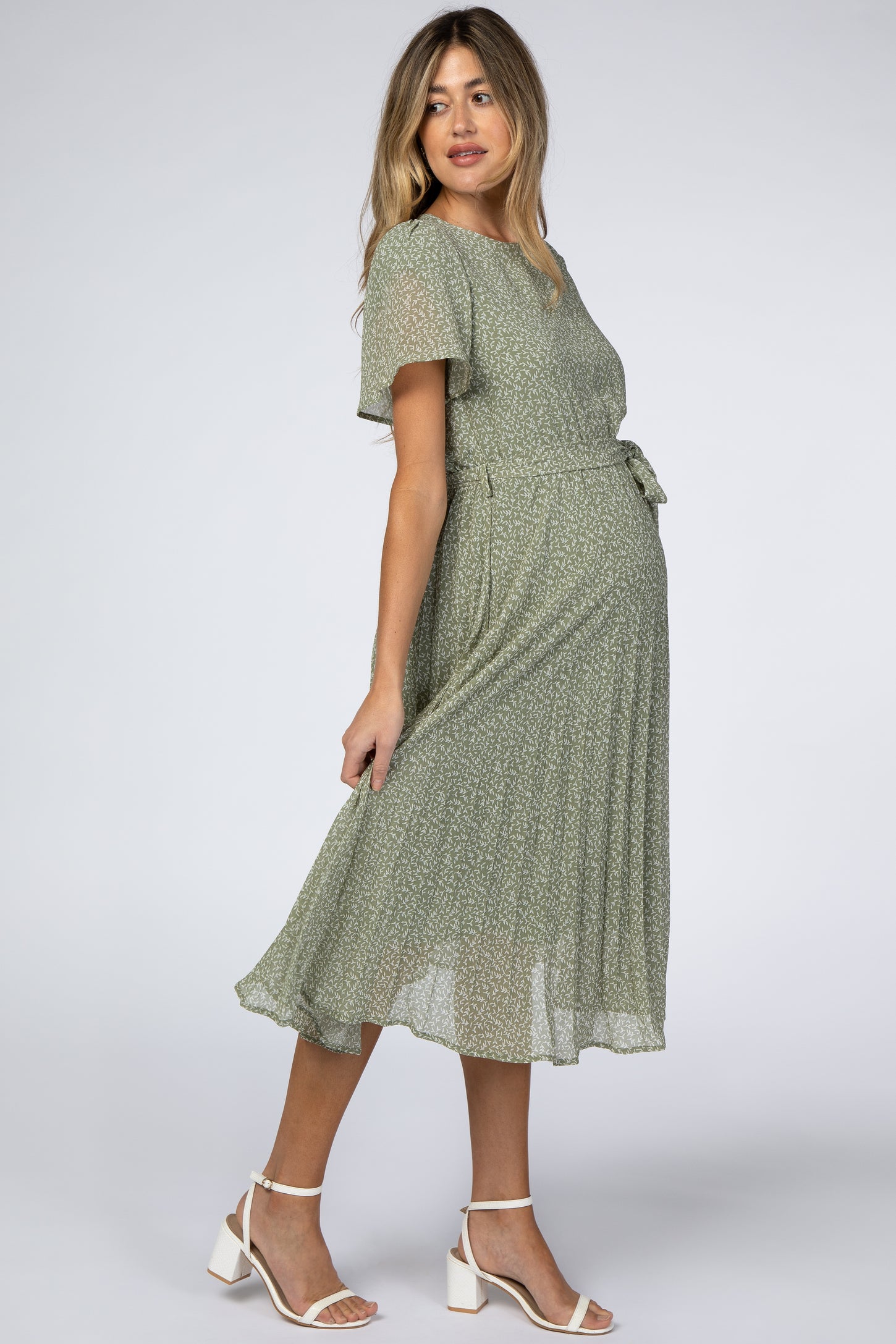 pregnant woman in a sage green floral maternity midi dress with short sleeves and white block heel sandals