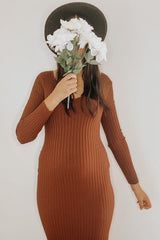 woman wearing a rust ribbed maternity dress, holding artificial flowers and displaying her baby bump