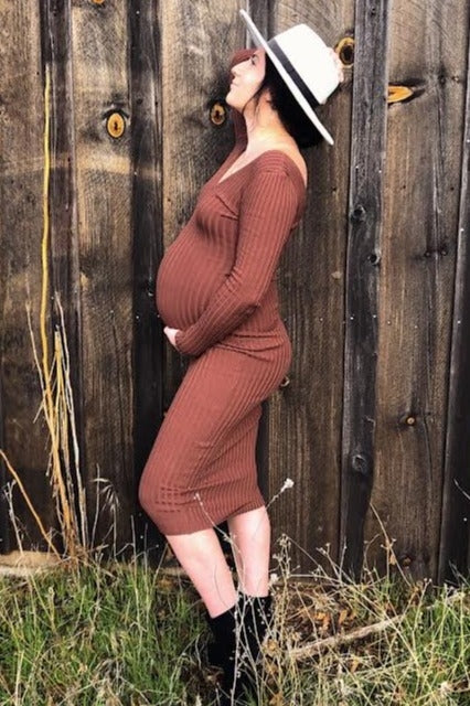 woman wearing a rust brown ribbed maternity dress, posing with a visible baby bump against a wooden background