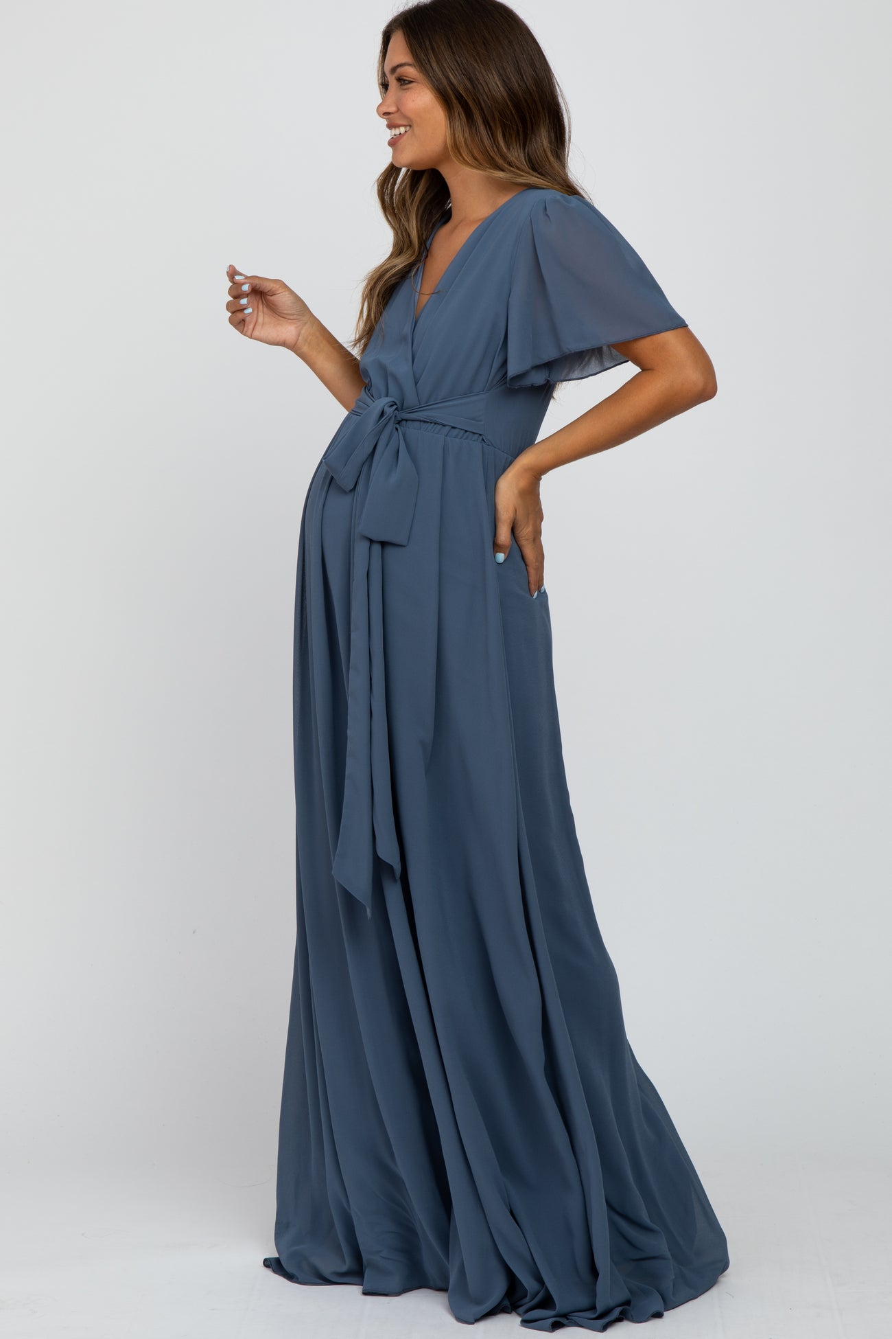 Pregnant woman wearing a dusty blue short sleeve maternity maxi dress with a waist tie