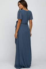 woman wearing a dusty blue short sleeve maternity maxi dress with a cinched waist and flowy skirt, viewed from the back