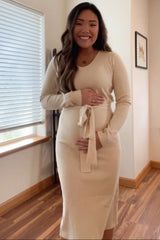 woman wearing a beige ribbed maternity dress with a tie at the waist and holding her baby bump